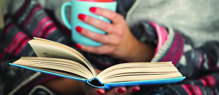 woman holding an open book and coffee mug
