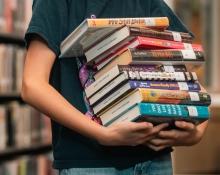Child holding a stack of nine books